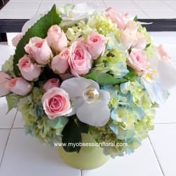 Pink roses and white orchids arranged with pale hydrangeas in a round vase