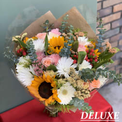 Mixed bouquet with sunflowers, white daisies, and pink roses wrapped in brown paper