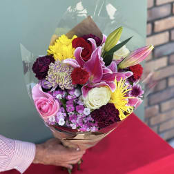 Handheld bouquet of mixed pink, yellow, white, and red flowers