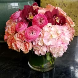 Pink and peach bouquet with roses, ranunculus, orchids, and hydrangeas in a glass vase