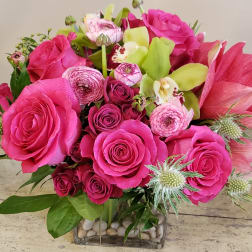 Bright pink roses and lilies arranged in a square glass vase.