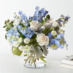 Arrangement of white roses, blue delphinium and hydrangea in a clear glass vase