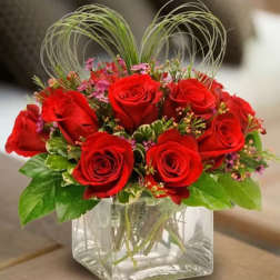 Red roses arranged in a clear square glass vase with decorative loops