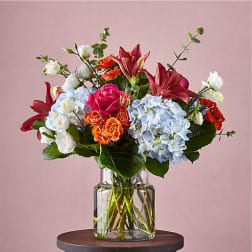 Mixed bouquet of roses, lilies, and hydrangeas in a clear glass vase