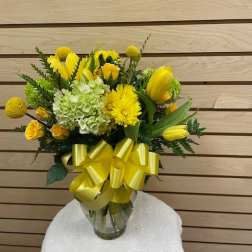Yellow floral bouquet in a glass vase with a large yellow ribbon