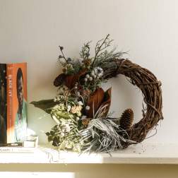 Rustic wreath with pinecones and dried florals beside stacked books