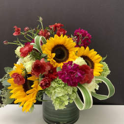 Mixed bouquet with sunflowers, hydrangeas, and red blooms in a dark vase