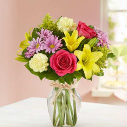 Bouquet of pink roses, yellow lilies, and purple daisies in a glass vase