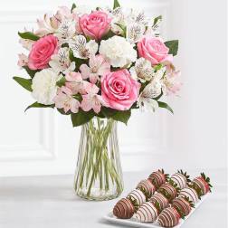 Pink and white bouquet in a clear glass vase with chocolate-covered strawberries on a tray