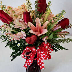 Bouquet of red roses and pink lilies in a dark vase with a heart ribbon