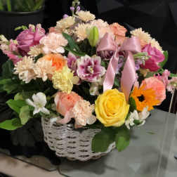Mixed flower arrangement in a white wicker basket with a pink ribbon