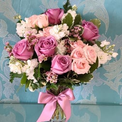 Bouquet of pink and lavender roses in a clear glass vase with a pink ribbon