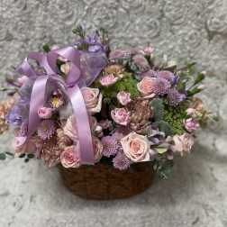 Basket arrangement of pink and lavender flowers with a purple ribbon
