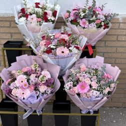 Five pastel flower bouquets arranged on a cart against a brick wall