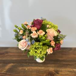 Compact arrangement of pink roses, peach carnations, green hydrangea, and berries in a white vase