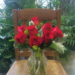 Red roses arranged in a clear glass vase on a wooden chair