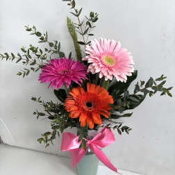 Gerbera daisies in pink, orange, and magenta in a vase with a pink ribbon