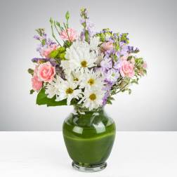 Mixed bouquet of white daisies, pink carnations, and lavender blooms in a clear glass vase with green lining.