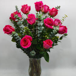 Bright pink roses arranged in a clear glass vase with eucalyptus