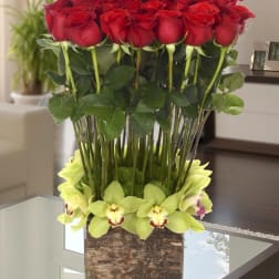 Tall arrangement of red roses with pale green orchids in a square glass vase