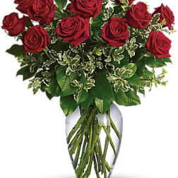 Arrangement of red roses in a clear glass vase with variegated foliage