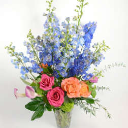 Tall bouquet of blue flowers with pink and peach roses in a clear vase
