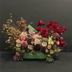 Mixed bouquet of red and blush roses with orchids in a green container