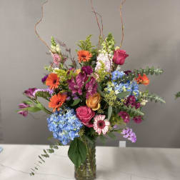 Mixed bouquet in a glass vase with bright orange, pink, blue, and purple flowers