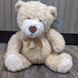 Cream teddy bear with a ribbon bow sitting on a wooden floor