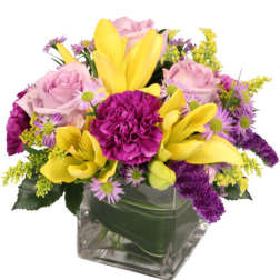 Mixed bouquet of yellow lilies, pink roses, and purple flowers in a glass vase