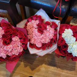 Three bouquets of red roses and pink carnations, one with white hydrangeas