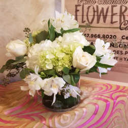 White roses and lilies arranged in a glass vase with pale green hydrangea.