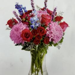 Mixed bouquet of red and pink roses with blue flowers in a glass vase