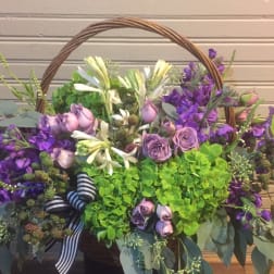Basket arrangement of purple and white flowers with a striped ribbon