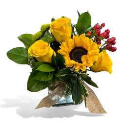 Yellow roses and a sunflower in a glass vase with a burlap ribbon