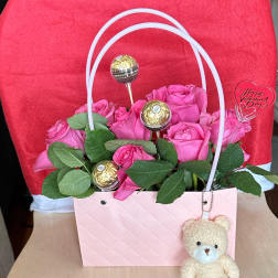 Pink roses in a gift bag with chocolates and a teddy bear charm