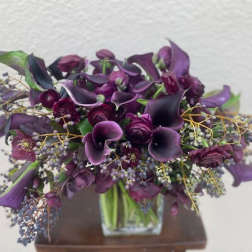 Purple calla lilies and roses arranged in a clear square vase