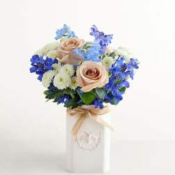 Bouquet of peach roses, blue flowers, and white daisies in a white vase
