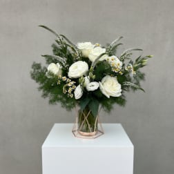 White roses and small daisies in a glass vase with greenery