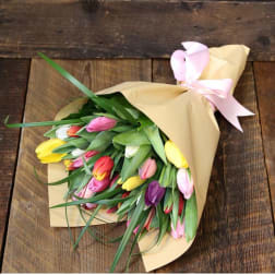 Bouquet of multicolored tulips wrapped in tan paper with a pink ribbon