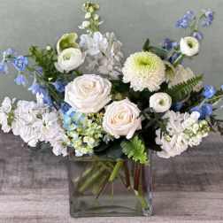 White and blue mixed flower arrangement in a square glass vase