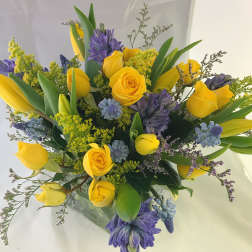 Arrangement of yellow roses and tulips with purple hyacinths in a clear glass vase