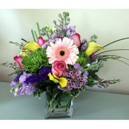 Mixed bouquet with pink gerbera daisies, roses, and purple flowers in a glass vase