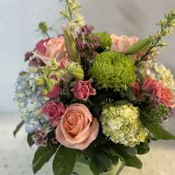Mixed bouquet of pink roses, hydrangeas, and green chrysanthemums in a glass vase