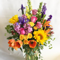 Colorful mixed bouquet in a clear glass vase with sunflowers, roses, tulips, and irises