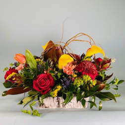 Mixed floral arrangement in a rustic rectangular container with red, yellow, and orange blooms