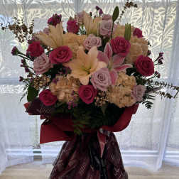 Large bouquet of pink roses, lilies, and hydrangeas in burgundy wrap