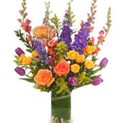 Colorful bouquet of roses, tulips, and purple spikes in a glass vase