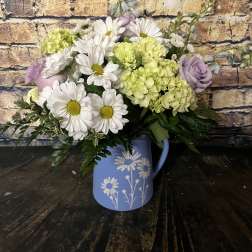 Bouquet of white daisies and pale green hydrangeas in a blue pitcher