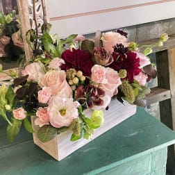 Pink and burgundy floral arrangement in a white wooden box